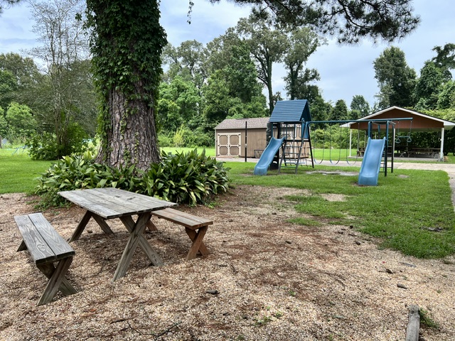 The exterior of Homeschool Clubhouse is shown. A picnic table sits in the foreground with a playset and covered pavillion with more picnic tables in the background. This is the secular co-op in Baton Rouge's playgound.